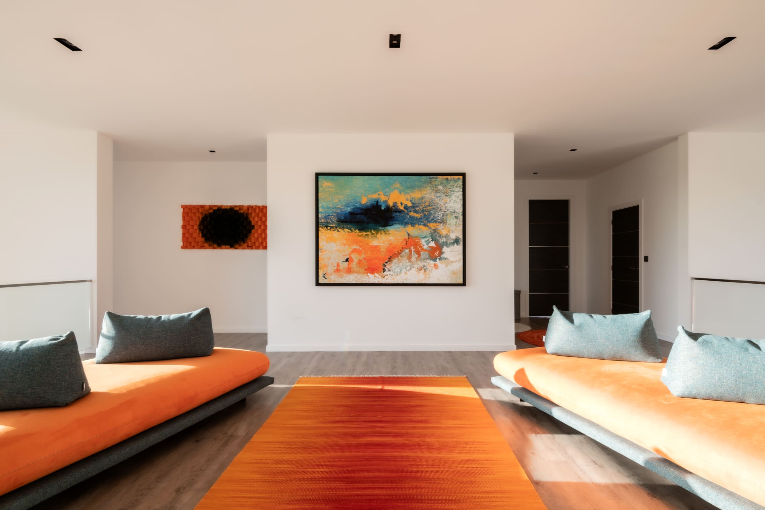 Modern living room with orange cushioned sofas, vibrant orange rug, and abstract artwork on white walls with wood flooring